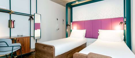 A modern hotel room with two single beds, a wooden desk, a chair, and a herringbone-patterned floor.