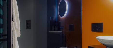 A modern bathroom with a glass partition, a round mirror, a white sink, and a towel hanging on the wall.