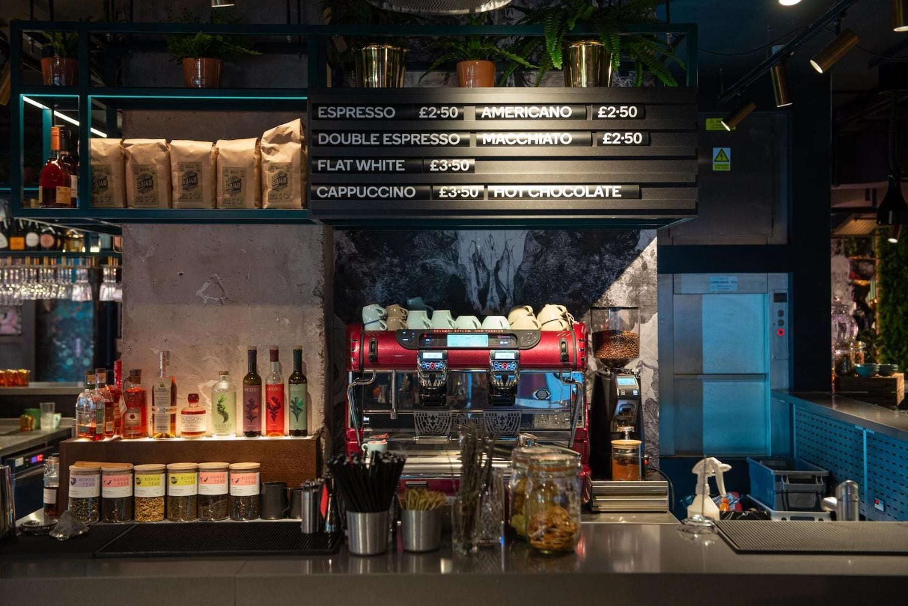 Una zona de bar con un menú de café, máquinas de espresso y varios frascos y botellas con ingredientes.