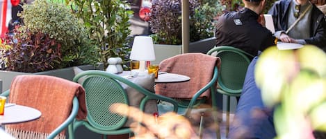 An outdoor café with green metal chairs and tables, a white lamp, and various plants.