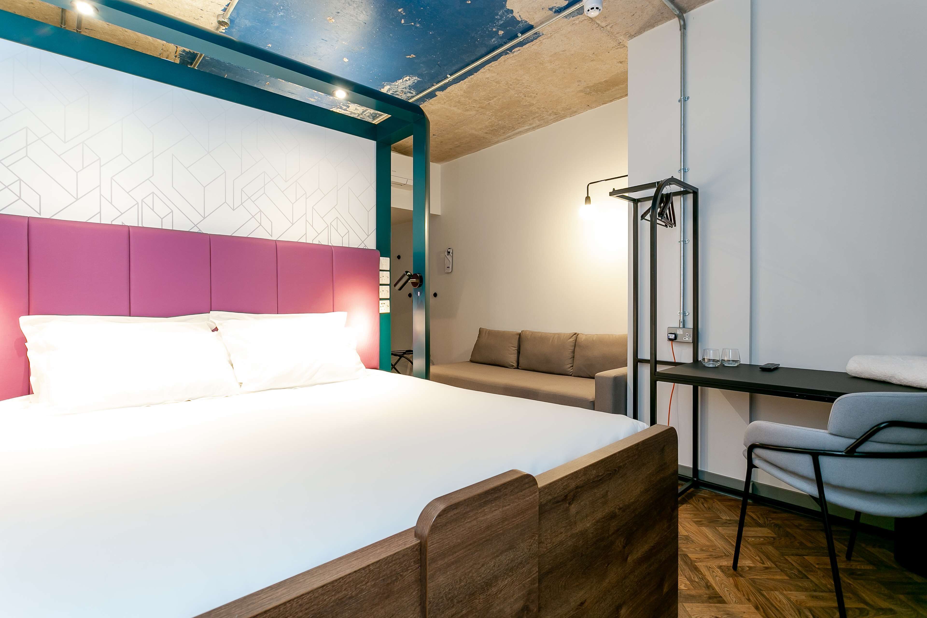 A modern hotel room with a large bed, a desk with a chair, a sofa, and a small table.
