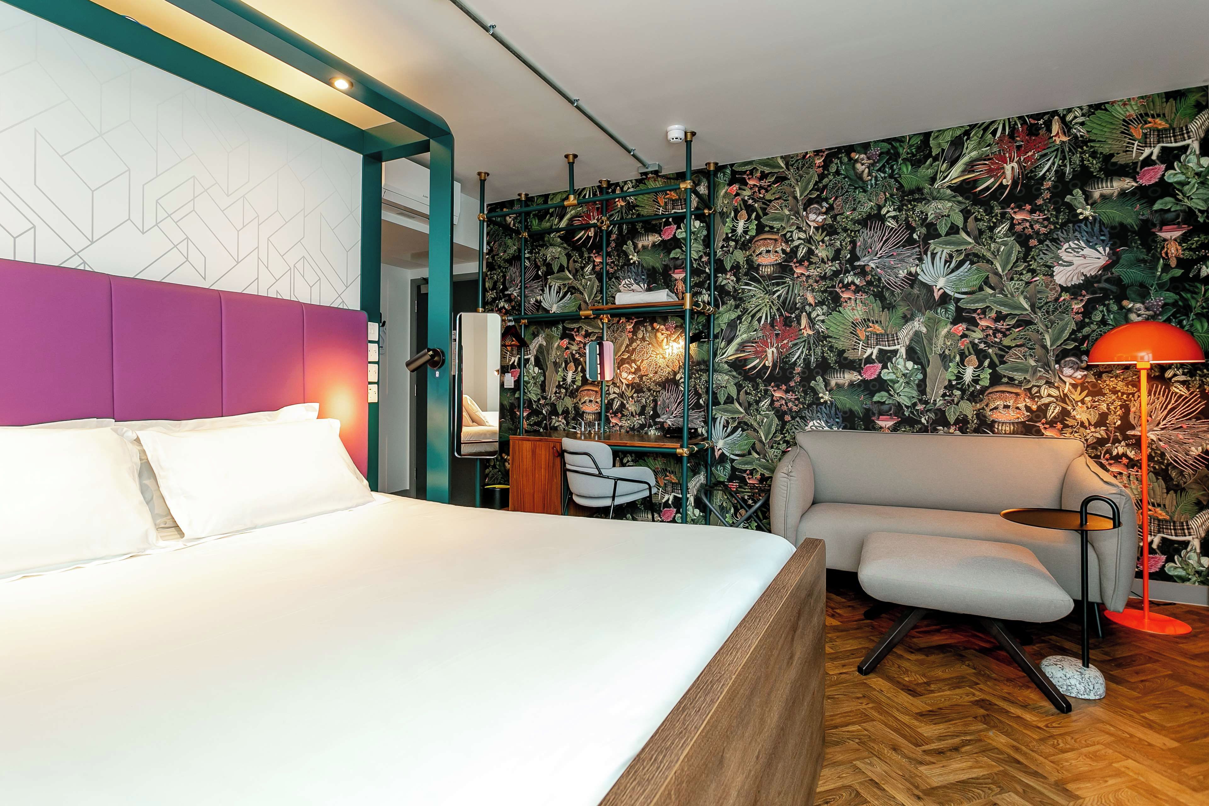 A modern hotel room with a large bed, a sofa, a desk, and a vibrant floral wallpaper.