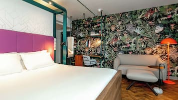 A modern hotel room with a large bed, a sofa, a desk, and a vibrant floral wallpaper.
