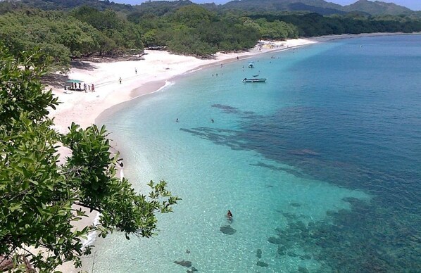 A beach with clear turquoise water, a sandy shore, and lush greenery in the background.