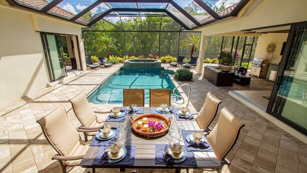 Un comedor con vista a la piscina, mobiliario exterior y un porche con paredes de vidrio.