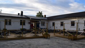 A covered outdoor seating area with tables and chairs, connected to a building with a red door and windows. - Skogmo Gjestgiveri (Overhalla)