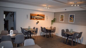 A dining area with multiple tables and chairs, a fish mural on the wall, and a plant hanging above the tables. - Skogmo Gjestgiveri (Overhalla)