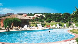 Una piscina con sillas de descanso, un edificio con techo de tejas y montañas al fondo.