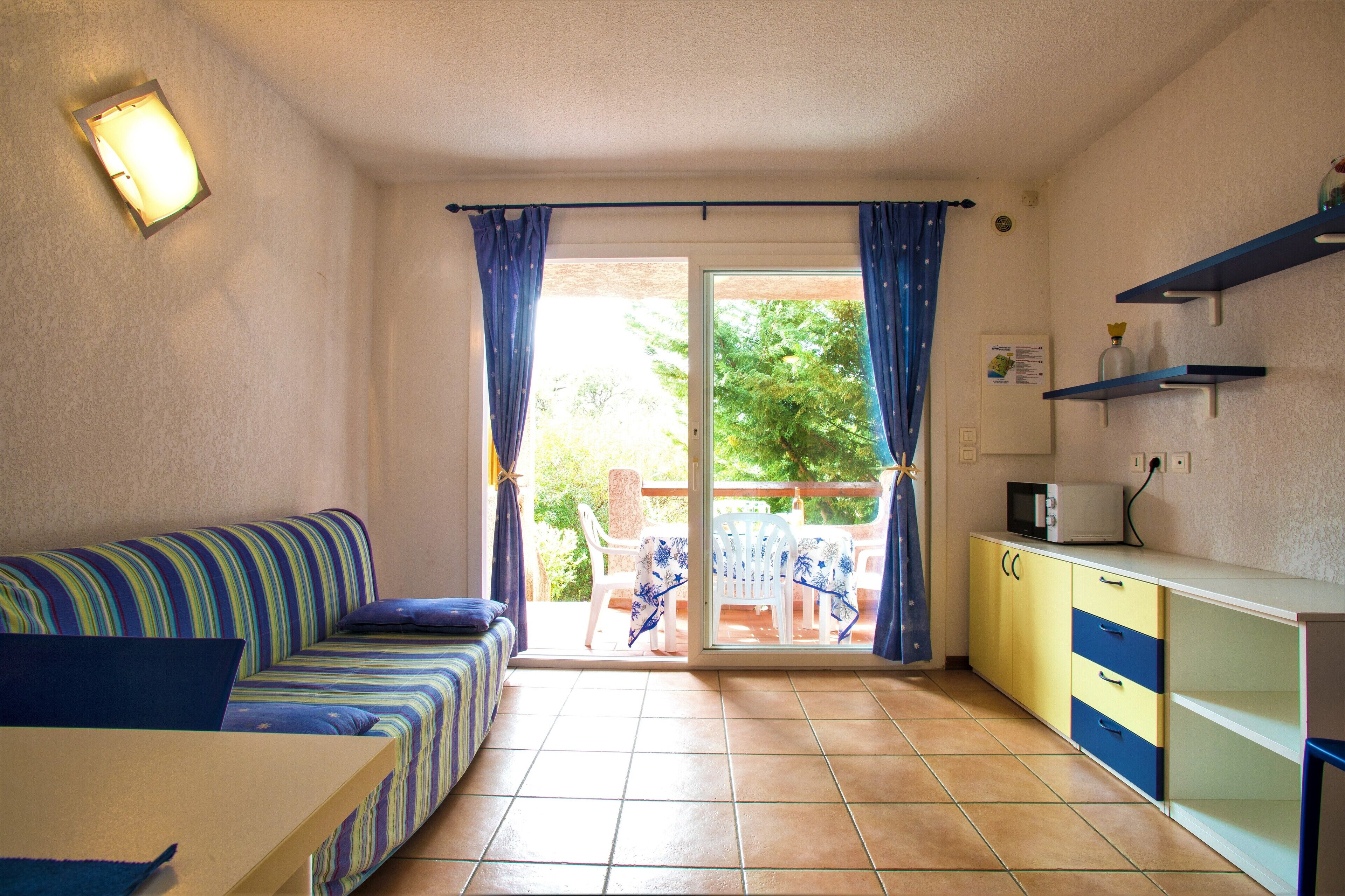 A small, bright room with a sofa, a table, and a kitchenette.