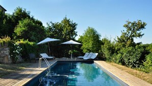 Ein Schwimmbecken mit Holzterrasse, zwei Liegestühlen und zwei Sonnenschirmen.