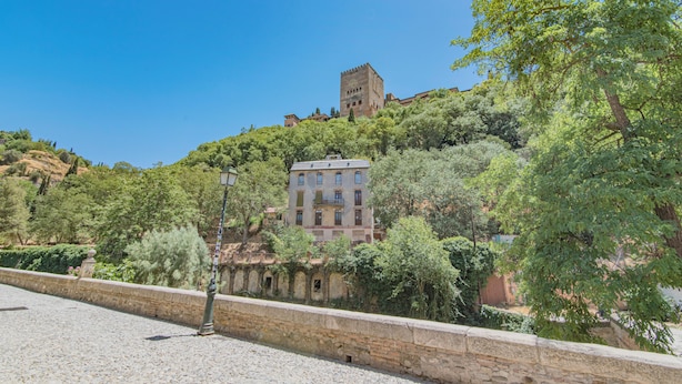 Un edificio histórico con una torre, rodeado de vegetación y un muro de piedra.