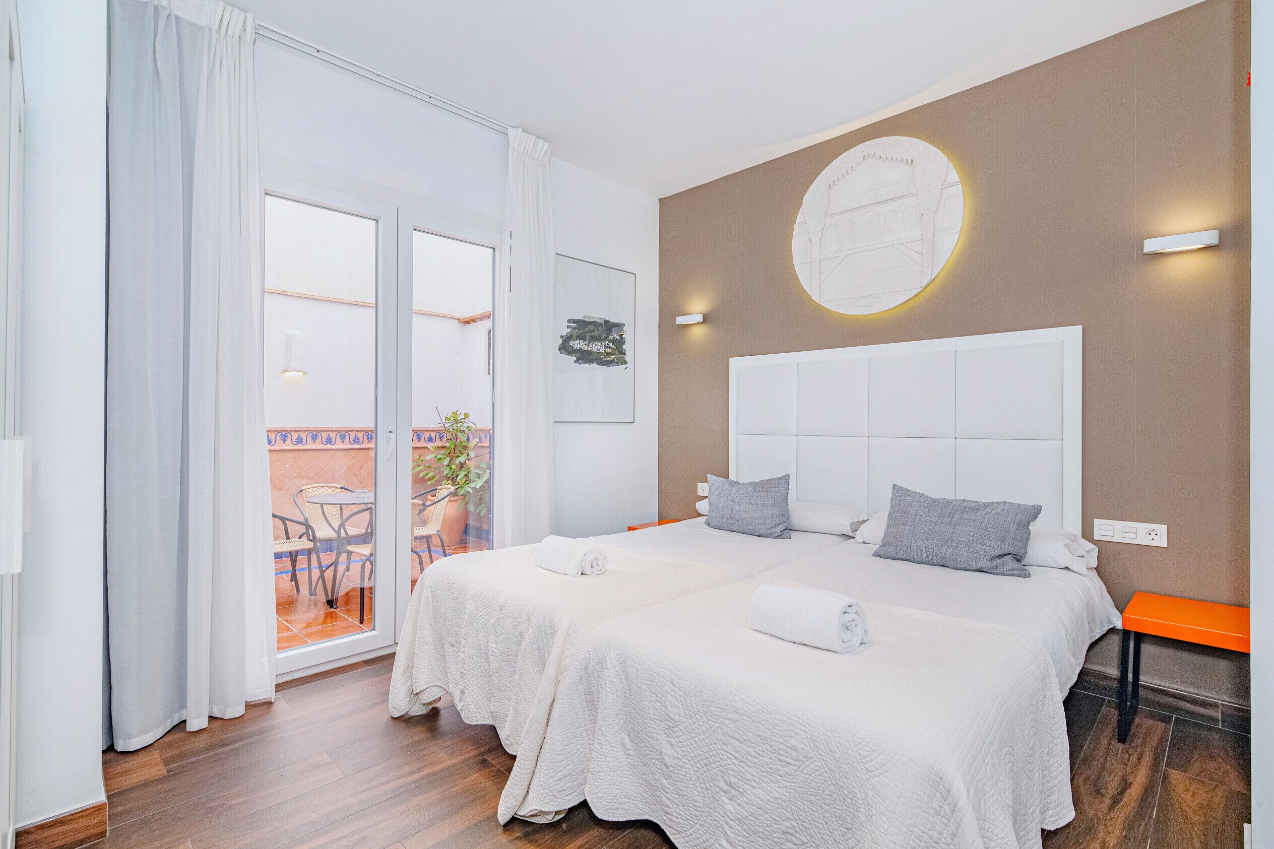 Een hotelkamer met twee bedden, een groot raam, een balkon en een wandlamp.