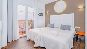 Habitación de hotel con dos camas, un ventanal grande, un balcón y una lámpara fijada a la pared.