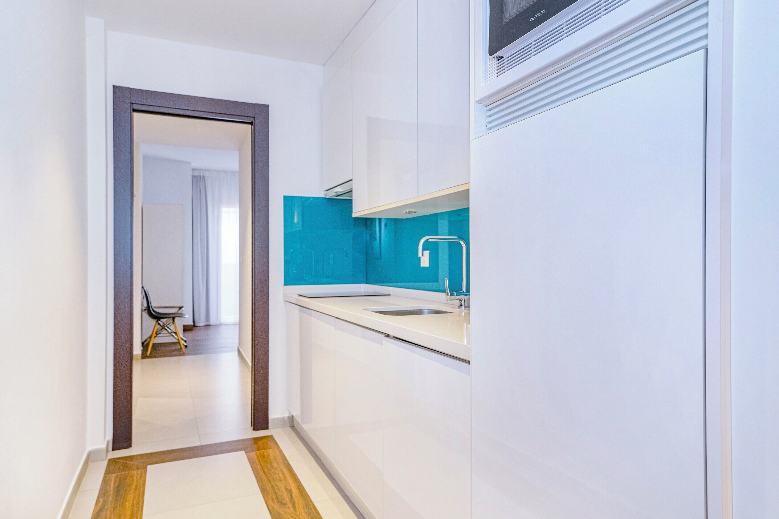 Una cocina moderna con armarios blancos, un salpicadero azul y un lavamanos de acero inoxidable.