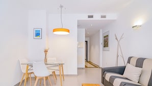 Una sala de estar moderna con un sofá, una mesa de comedor con sillas, una lámpara colgante y un pequeño banco de madera.
