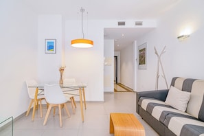 Ein modernes Wohnzimmer mit einer Couch, einem Esstisch mit Stühlen, einer Pendelleuchte und einer kleinen Holzbank.