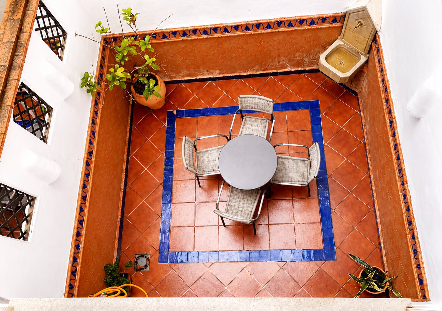 A courtyard with a tiled floor, a round table with chairs, a potted plant, and a toilet.