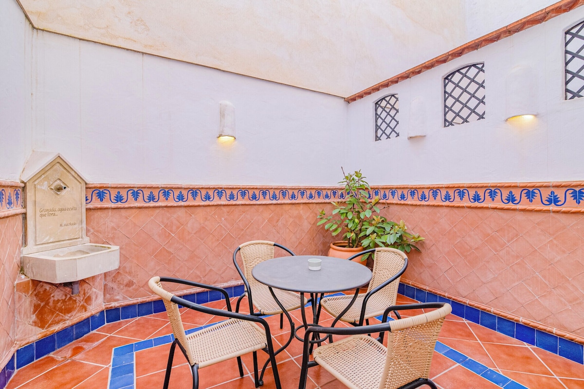 Eine Terrassengrundstück mit Fliesenboden, Korbstühle, einem Tisch, einem Blumentopf, einer Wandleuchte und einer dekorativen Plakette.