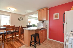 A kitchen with wooden cabinets, a white refrigerator, a microwave, and a dining area with chairs and a table.