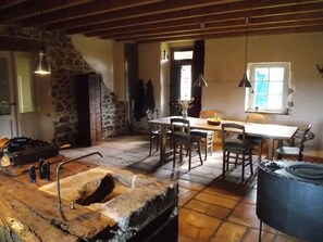 A rustic dining area with stone walls, a wooden table, and chairs. There is a stone sink and a large black barrel in the foreground. - La Rosière 2. A heavenly place in the midst of nature, peace and quiet. (Auzelles)