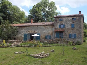 A stone building with a tiled roof, multiple windows with shutters, and a small garden area with a white umbrella. - La Rosière 2. A heavenly place in the midst of nature, peace and quiet. (Auzelles)