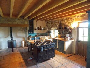 A rustic kitchen with a large stove, stone walls, and wooden beams. - La Rosière 2. A heavenly place in the midst of nature, peace and quiet. (Auzelles)