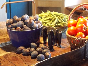 A kitchen counter with a bowl of plums, a basket of green beans, a bowl of tomatoes, and a knife block. - La Rosière 2. A heavenly place in the midst of nature, peace and quiet. (Auzelles)