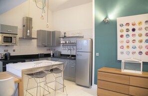 A modern kitchen with stainless steel appliances, a white countertop, and a bar area with metal chairs.