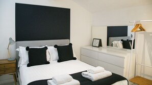 Una camera d'albergo moderna con un letto grande, un comodino con una lampada, una cassettiera e uno specchio.