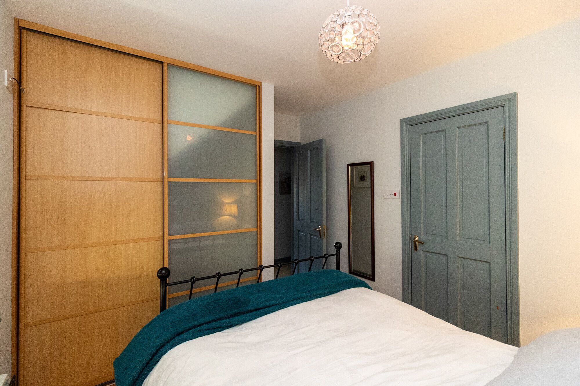 A bedroom with a bed, a wardrobe, a door, and a hanging light fixture.