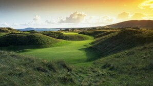Un parcours de golf avec des collines ondoyantes et un coucher de soleil en arrière-plan.