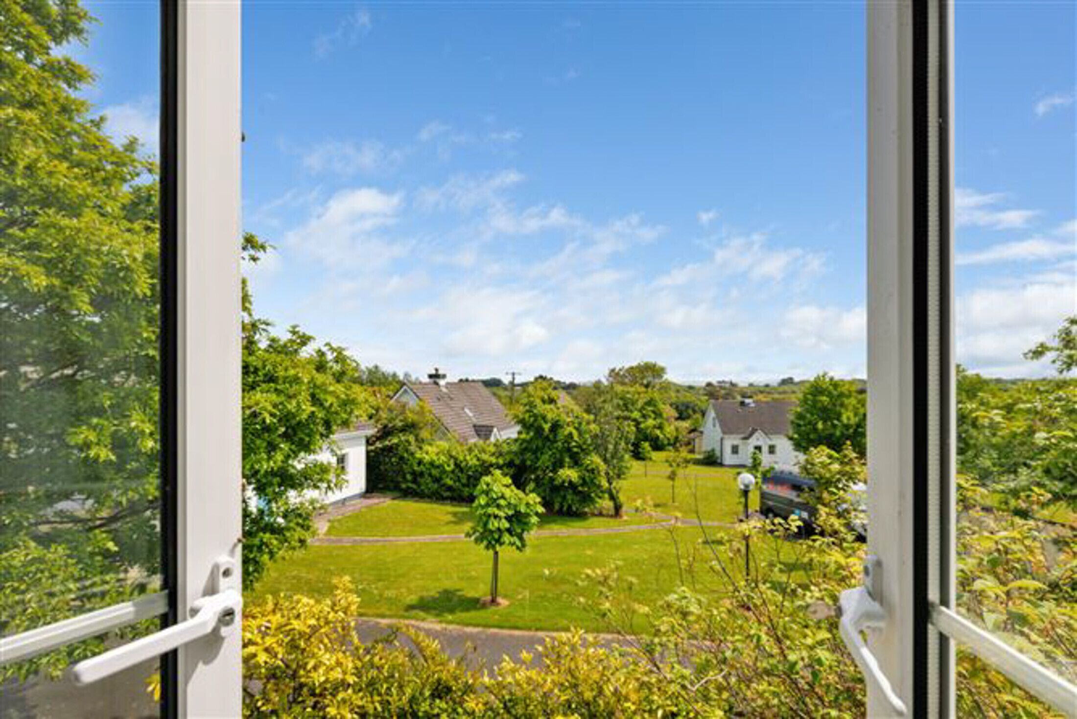A view through a window of a residential area with houses, a lawn, and trees.