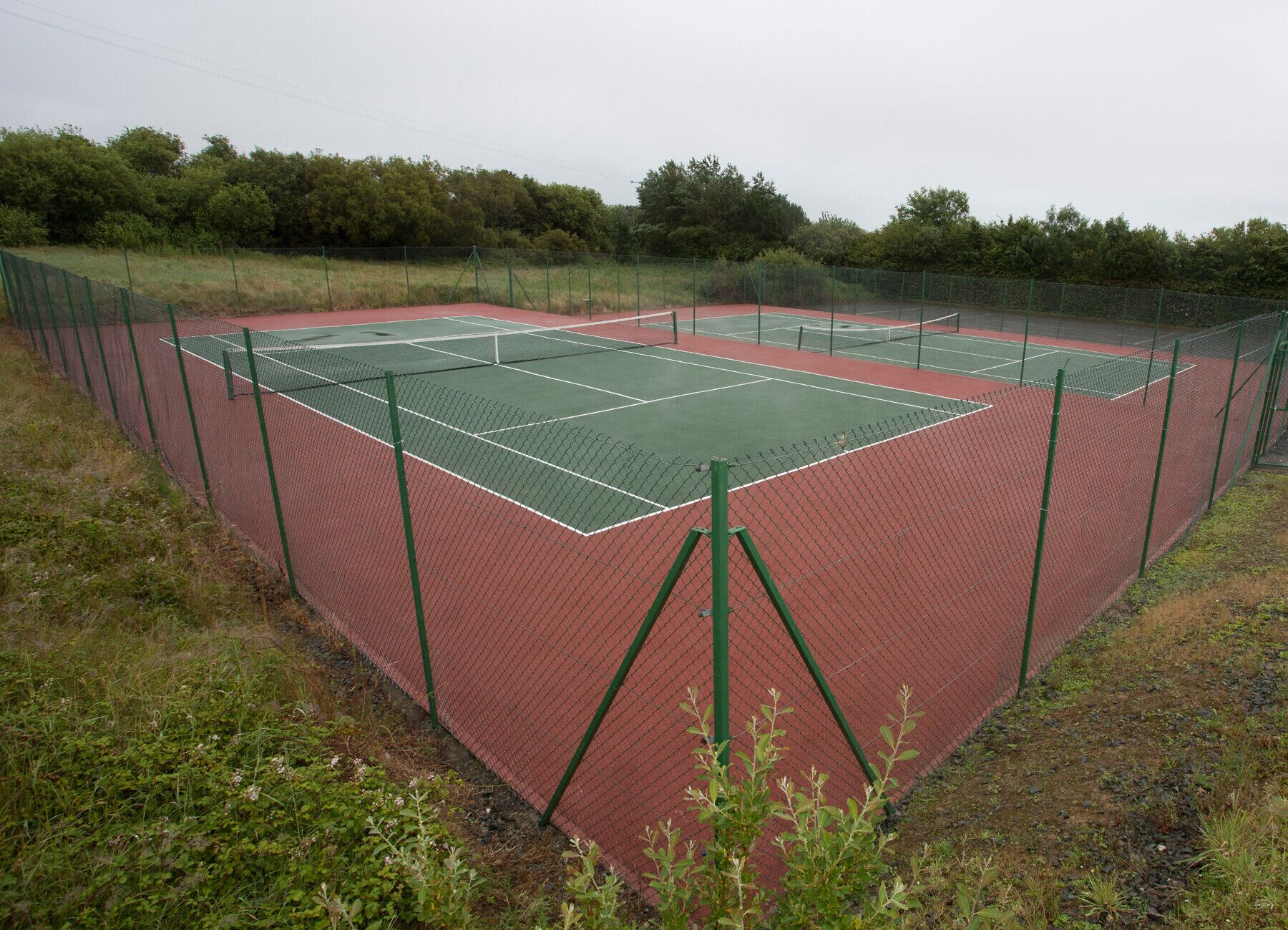 A tennis court with a green net, surrounded by a green fence.