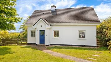 A single-story white house with a blue door, a chimney, and a small front yard with a wooden fence.