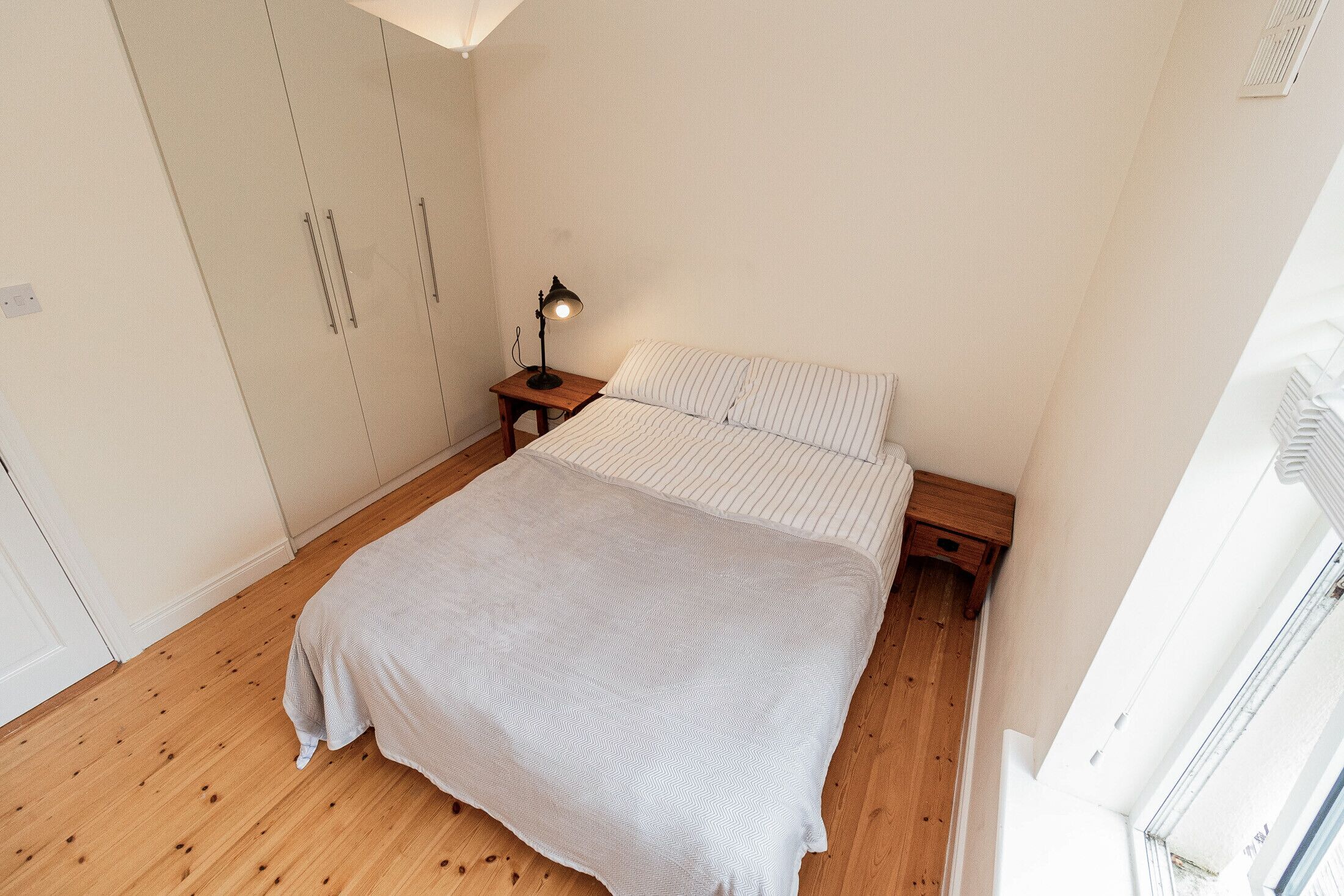 A bedroom with a bed, a nightstand, a lamp, and a wardrobe.