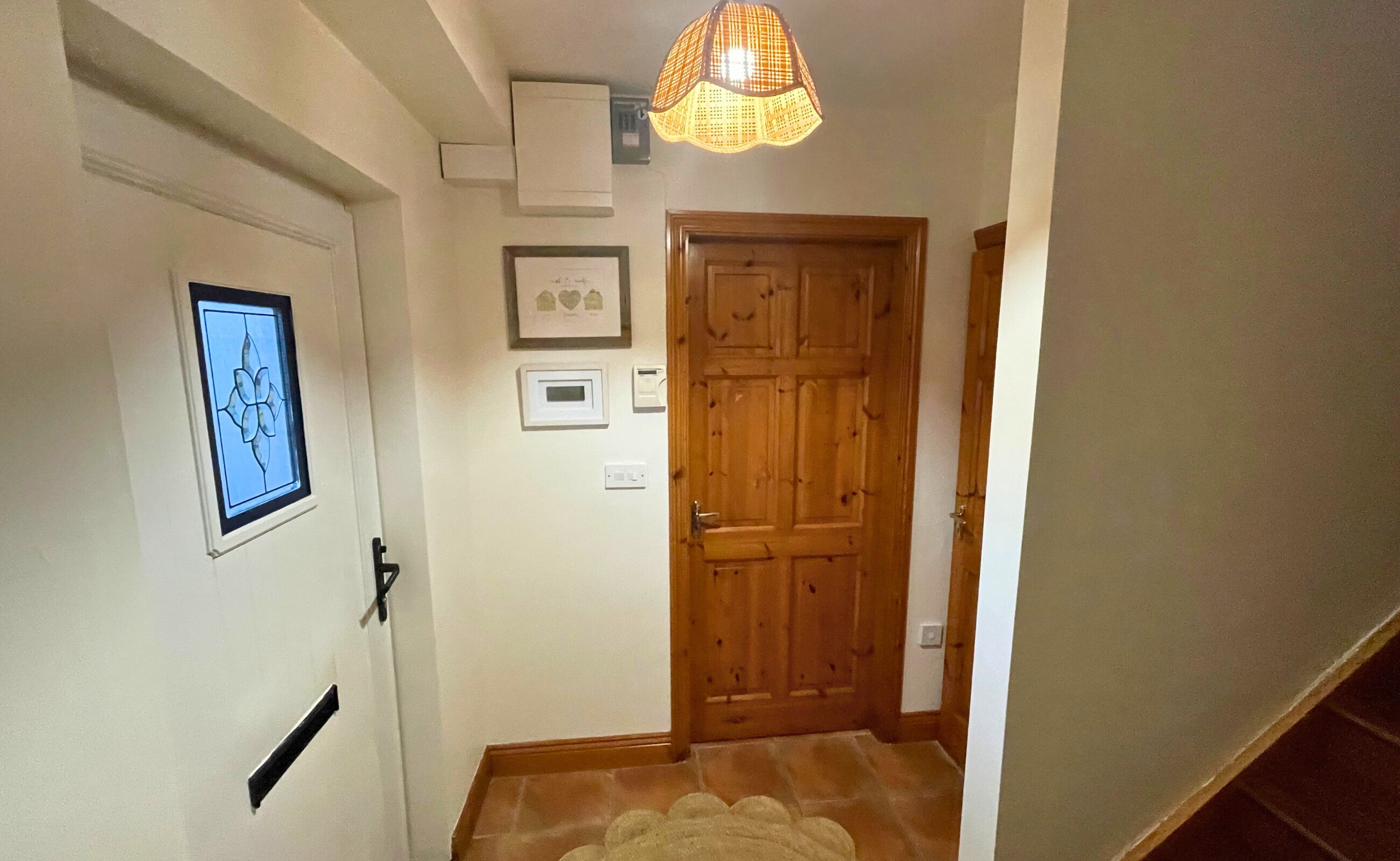 Een gang met een houten deur, een lijst met een afbeelding en een hanglamp.