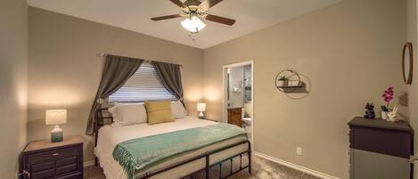 A bedroom with a bed, nightstand, ceiling fan, and a dresser.