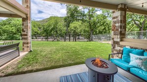 A covered patio area with a stone pillar, a fire pit, a blue sofa, and a bench. - Riverfront Fun Rg 111 2 Bedroom Condo by RedAwning (New Braunfels)