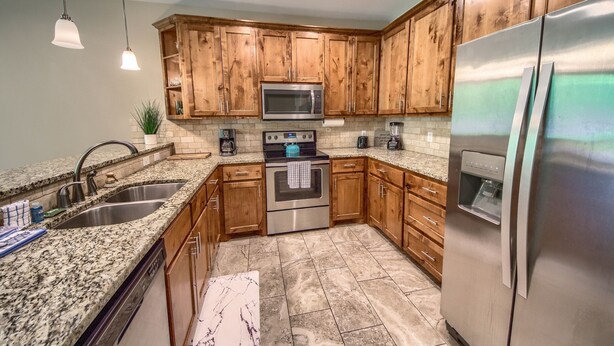 A kitchen with wooden cabinets, stainless steel appliances, granite countertops, and a built-in oven. - Riverfront Fun Rg 111 2 Bedroom Condo by RedAwning (New Braunfels)