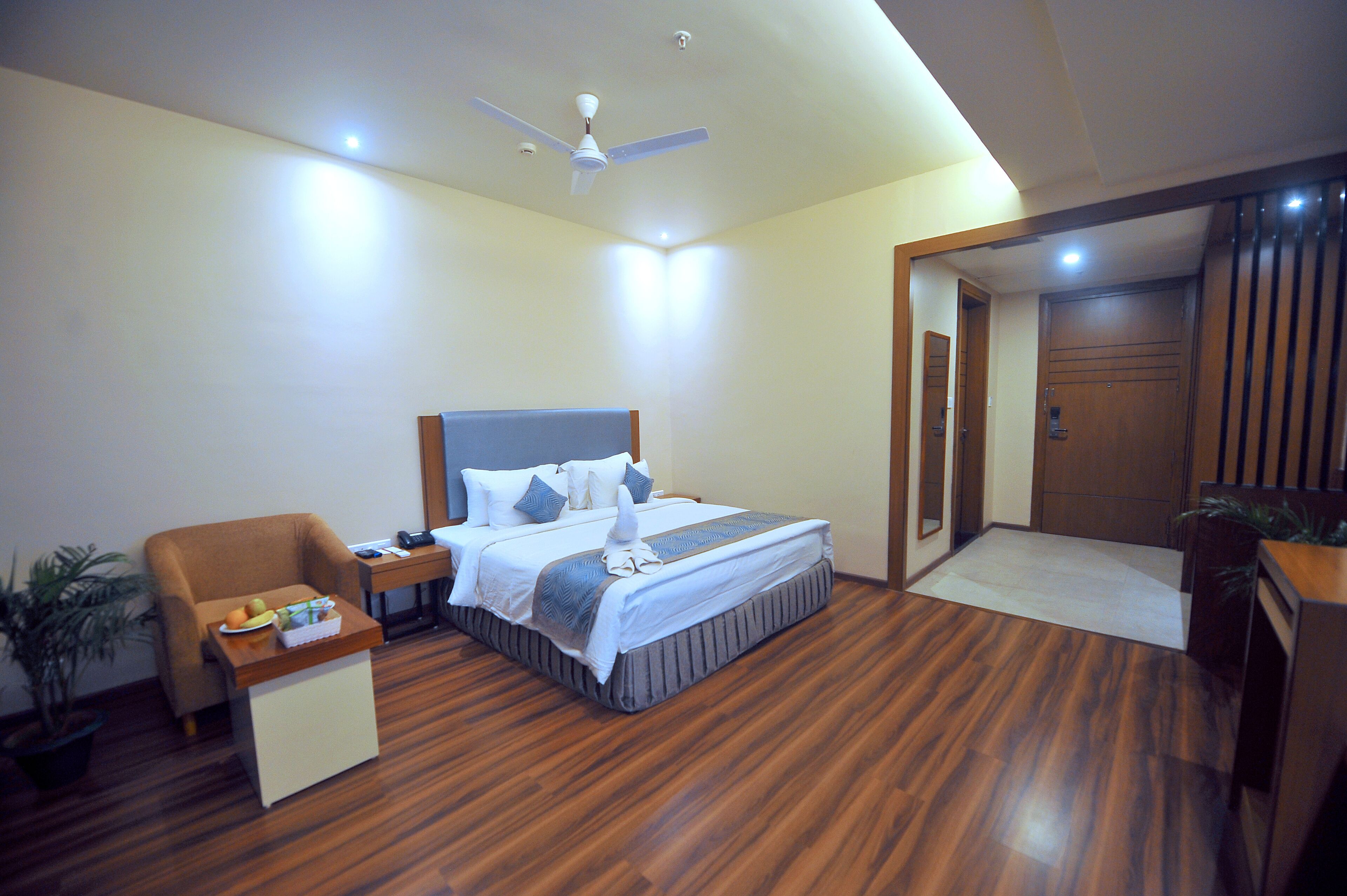 Una habitación de hotel con cama, mesita de noche, silla y ventilador de techo.