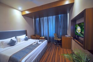 Habitación de hotel con una cama grande, un escritorio con silla, un televisor y una ventana con cortinas.
