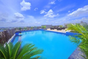 A rooftop swimming pool with clear blue water, surrounded by palm trees and a view of the cityscape. - Pipul Padmaja Premium and Convention (Bhubaneshwar)