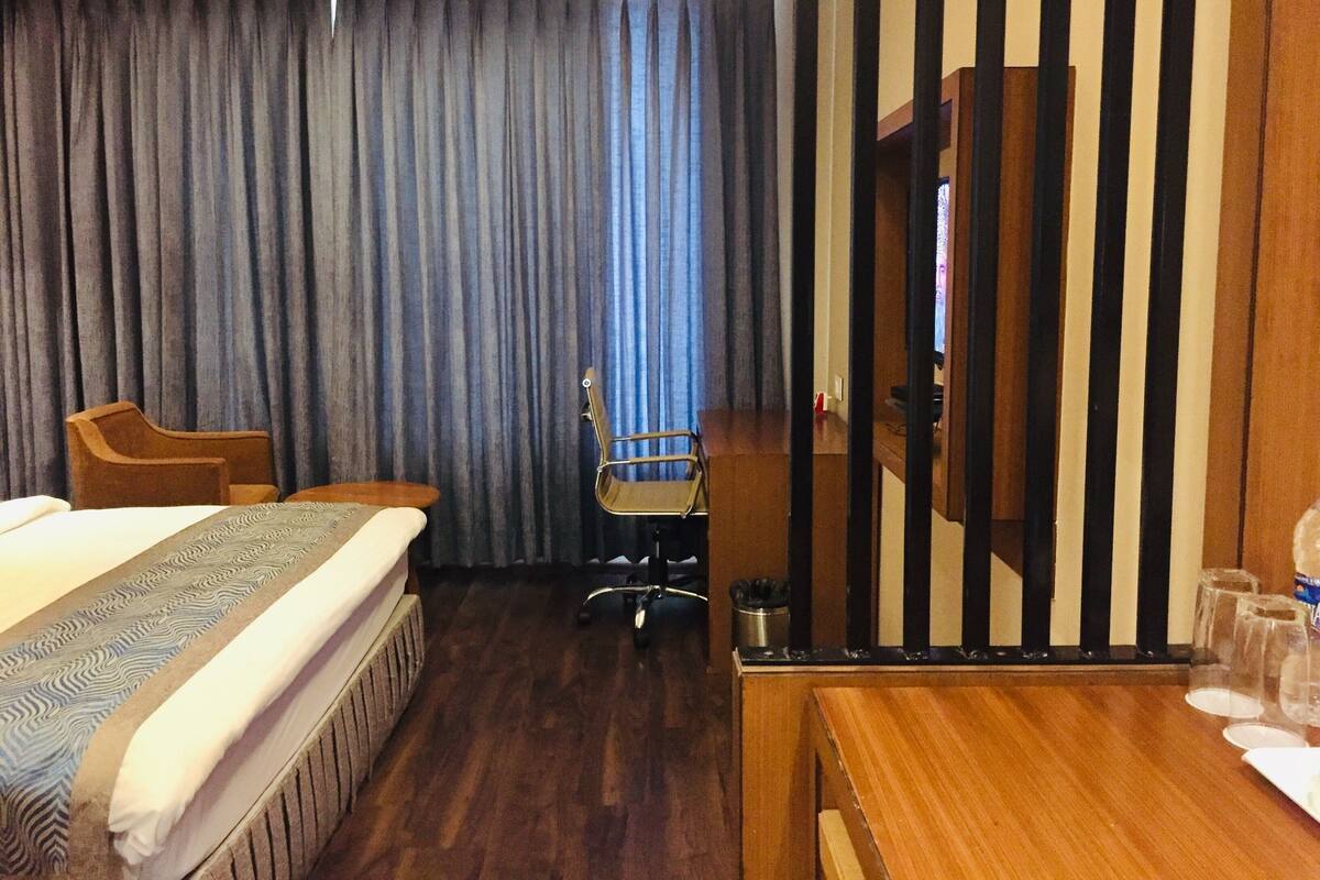 A hotel room with a bed, a desk, a chair, a television, and a curtain.