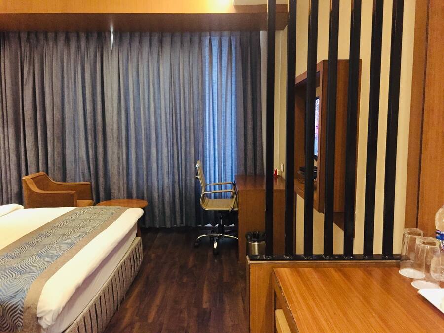 A hotel room with a bed, a desk, a chair, a television, and a curtain.