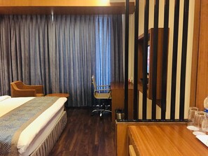A hotel room with a bed, a desk, a chair, a television, and a curtain. - Pipul Padmaja Premium and Convention (Bhubaneshwar)