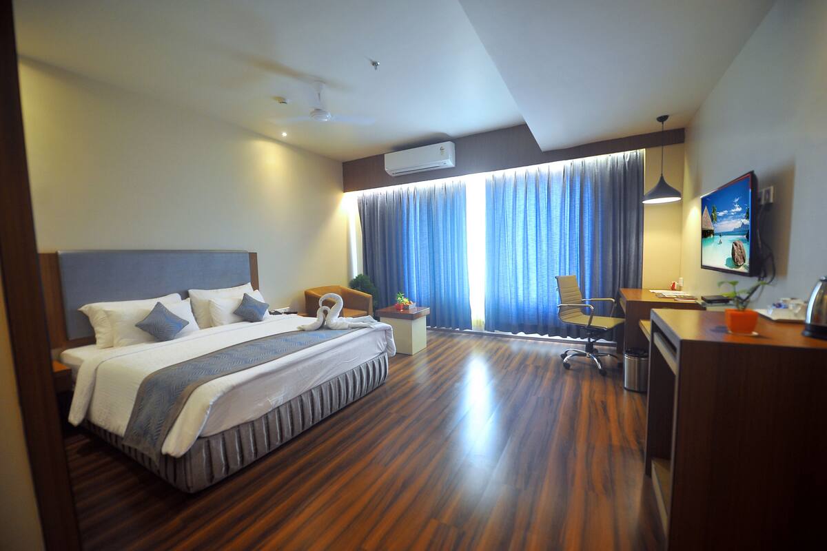 A hotel room with a large bed, a desk, a chair, and a window with curtains.