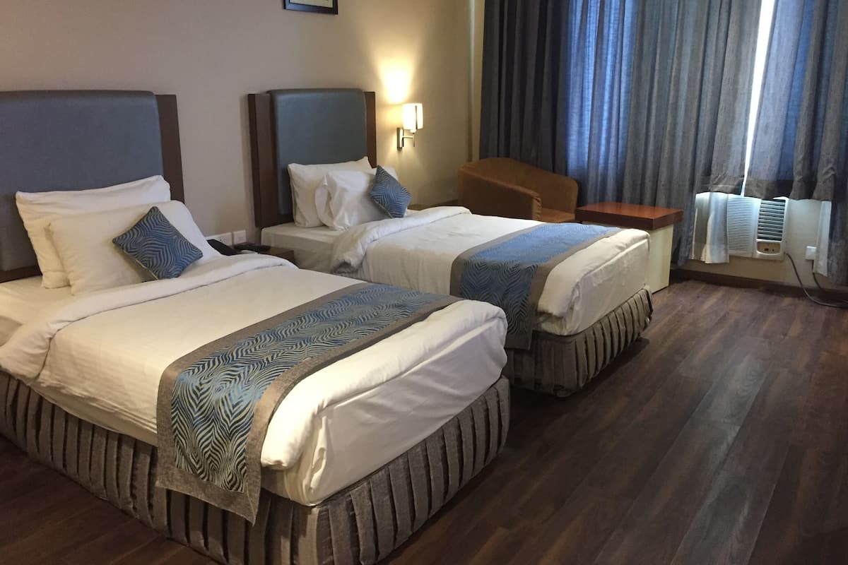 A hotel room with two beds, a nightstand, a chair, and a window with curtains.