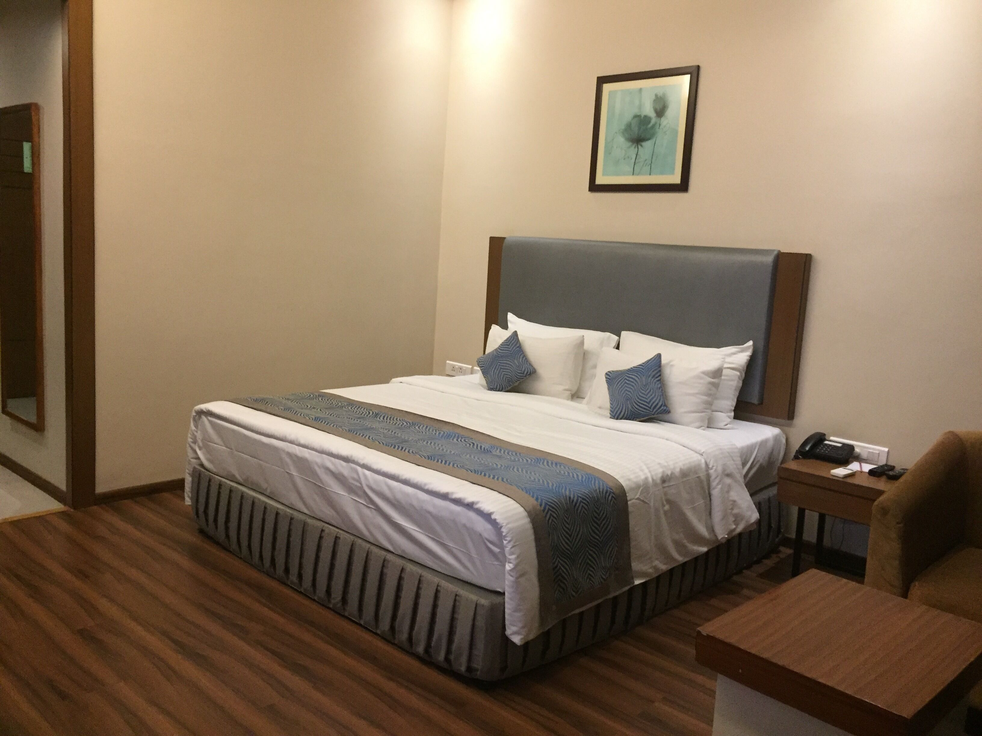Habitación de hotel con una cama grande, suelo de madera, mesita de noche con un teléfono y una silla.