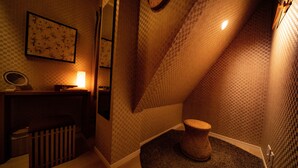 A small, dimly lit bathroom with a checkered wall pattern, a round wicker stool, and a mirror on a wooden vanity.