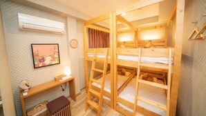 A room with bunk beds, a desk with a mirror, a small table, and an air conditioner.